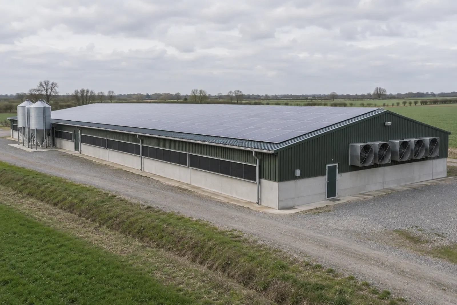 A long poultry unit with a broad shallow roof covered in solar panels, feed silos at one end